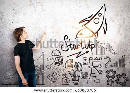 Side view of young businessman pointing at concrete wall with rocket sketch. Start up concept Royalty-Free Stock Photo #663888706