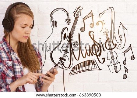 Portrait of attractive casual european girl listening to music on white brick background with. Hobby/passion concept