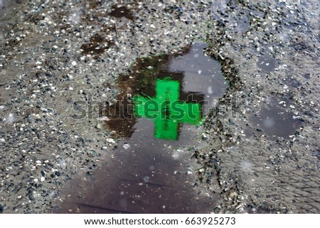 Neon cross, pharmacy sign, with burning lights in the form of a heart reflected in a puddle on the asphalt in rainy weather. For wallpaper, advertising, design, covers, background, textures.