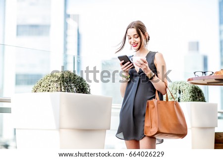 Young businesswoman using phone standing on the terrace with great cityscape view during the breakfast in Frankfurt