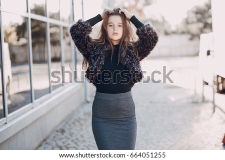 girl with long hair and skirt stands near a high wall