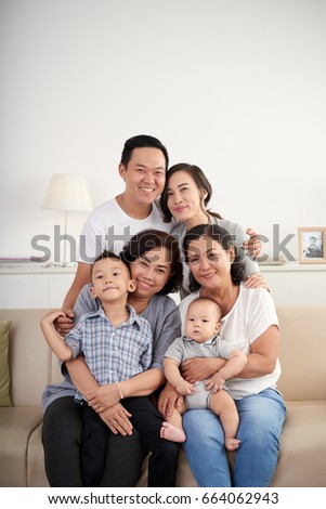 Portrait of big Asian family posing for photo at home sitting on sofa, all smiling happily looking at camera
