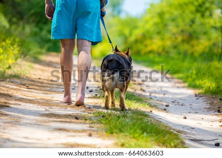 Man walking barefoot back to camera with a dog on dirt road in summer