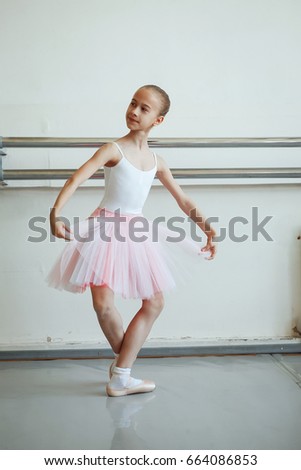 Cute little ballerina in pink ballet costume and pointe shoes is dancing in the room. Kid in dance class. Child girl is studying ballet. Copy space.