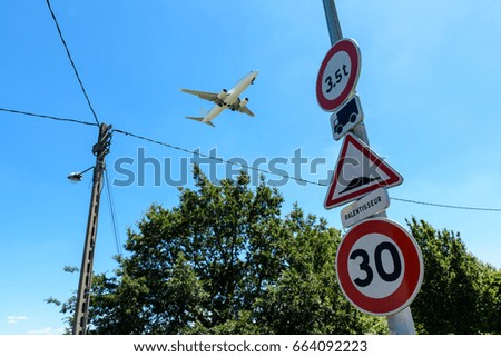 An airliner in landing approach flying above a residential area with roadsigns in the foreground.