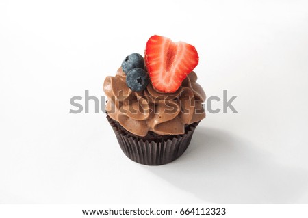 Chocolate cupcake with whipped chocolate cream, decorated fresh strawberry, blueberry on white background. Picture for a menu or a confectionery catalog. Top view.
