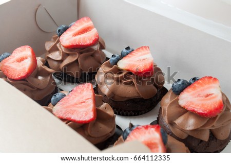 Chocolate cupcakes with whipped chocolate cream, decorated fresh strawberry, blueberry on white background in box. Picture for a menu or a confectionery catalog.