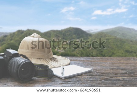 Camera with cap, notebook and pen on wooden table with mountain and sky background, Travel concept. Travel Accessories.