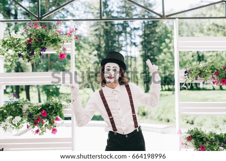 Pantomime theater artist posing near the pot of summer flowers.