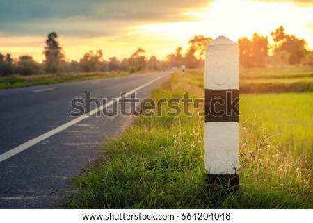Mile stone on beside dirt road and sunset time background , a kilometer stone on the road and Grass and sunset is back ground