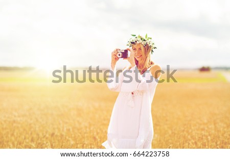 nature, summer holidays, vacation and people concept - happy woman in wreath of flowers taking picture with film camera outdoors