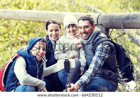travel, tourism, hike, technology and people concept - happy family with backpacks taking picture by smartphone and selfie stick in woods