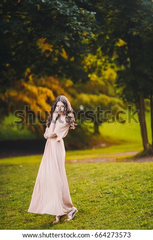Portrait of a beautiful attractive lady of a young slender brunette girl with long dress walking through a green park with flowers at sunset lifestyle outdoor