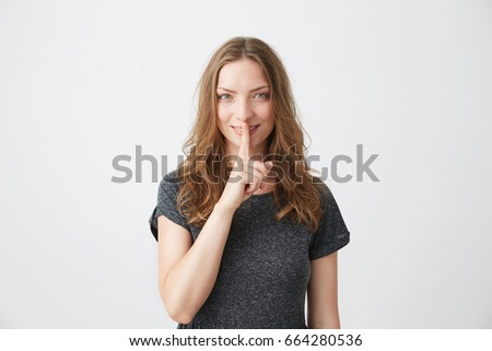 Portrait of young pretty tender girl smiling looking at camera straight showing keep silence over white background.