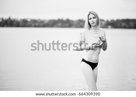 Portrait of a fantastically looking tall model wearing t-shirt and bikini walking in lake. Black and white photo.