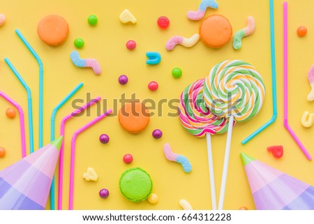 Sweets for birthday including lollipop, macarons and drops on yellow background top view