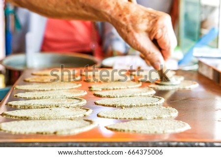 Old man's hand is making sweets Thai Crispy Pancake for customers. In picture he putting  dough sheets on hot pan.