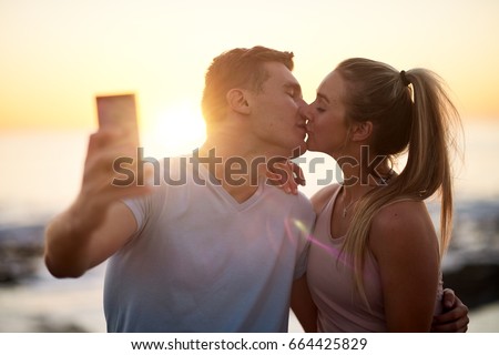 Romantic couple on date take a selfie with the sunset, kissing by the ocean