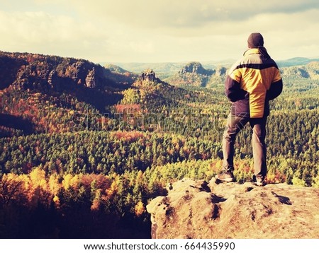 Man stay on sharp rock peak. Satisfy hiker enjoy view. Tall man on rocky cliff watching down to landscape. Vivid and strong vignetting effect.