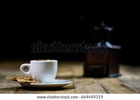 Freshly brewed coffee in mugs on a wooden table with a mill on a black background