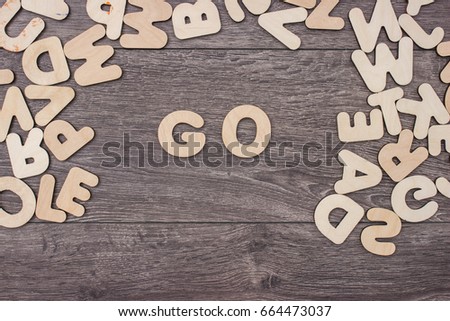 Word Go made with wooden letters next to a pile of other letters over the wooden board surface composition