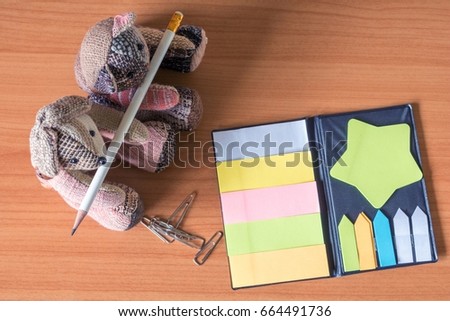 Empty colourful adhesive paper, teddy bear and cat doll show pencil on desk background.