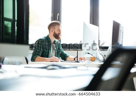 Picture of young handsome man work in office using computer. Looking aside.