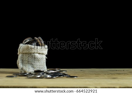 Coins overflow from hemp sack on wood table. Black background. Copy space. Conceptual savings or investing money for growing your business and finance.