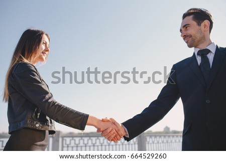 A young successful man gladly shakes hands with the business lady on the street