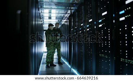 In Data Center Two Military Men Work with Open Server Rack Cabinet. One Holds Military Edition Laptop. Royalty-Free Stock Photo #664639216