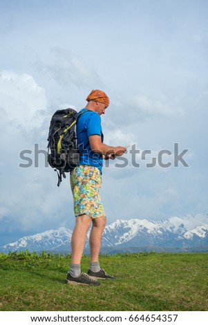 Adventurer is walking along the mountain ridge, holding the tablet computer in his hands - travel in  modern world.