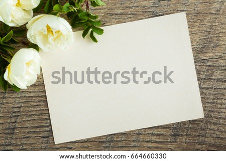 White roses with blank greeting card on the wooden table. Fresh flowers.