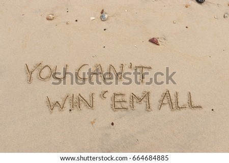 Handwriting  words "YOU CAN'T WIN'EM ALL" on sand of beach.