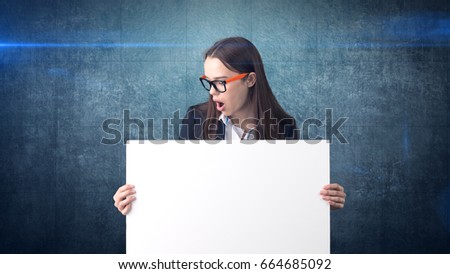 Surprised Business woman portrait with blank white board on blue isolated . Female model with long hair in glasses.
