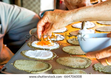 Old man's hand is making sweets Thai Crispy Pancake for customers. In picture he putting  golden threads dessert on top of sweet cream and dough sheets.