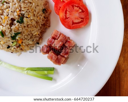 This is popular Thai food, easy to cook, less time and tasty. Top view picture of pork fried rice on white plate above wooden  table.