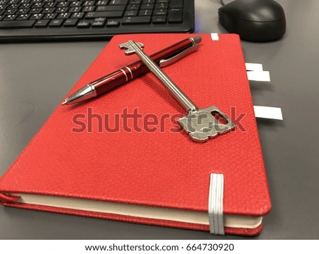 the key and pen on the red note book with office desk
