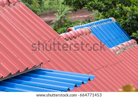 Red and blue carved tile of house roofs with slight falling raindrops and green leaves background, durable metal roof sheets
