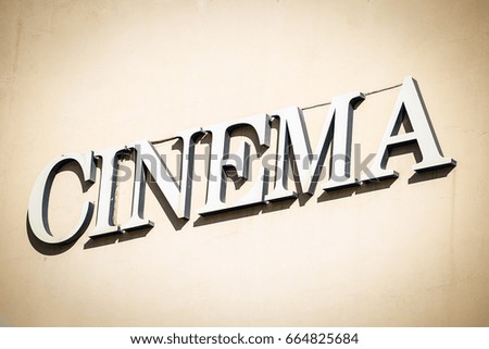 Front view of sign with letters pointing to cinema on wall. 