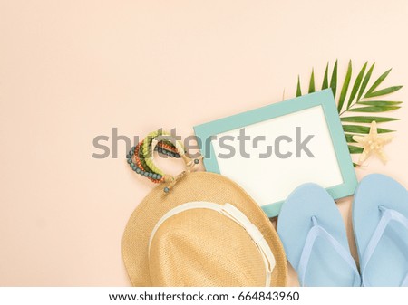 Empty frame and summer holidays items on creme background. Straw hat, blue flip flops and wood bracelet. Selective focus. Place for text. Flat lay, top view