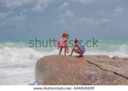Splashes of waves on large stones on the sea. Girls girlfriends on large stones on the beach play with a spray