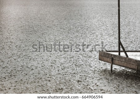 Lonely fishing pier on a lake under heavy shower rain. Bad weather. Bad mood concept. Gloomy colors