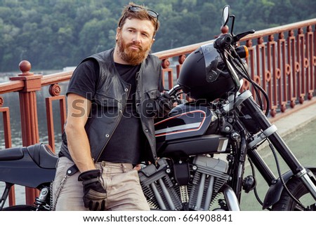 Bearded redhead biker with beard in leather jacket near bike. 