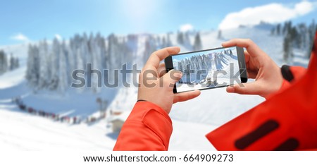 Man at the top of mountain taking photo of ski slope with phone