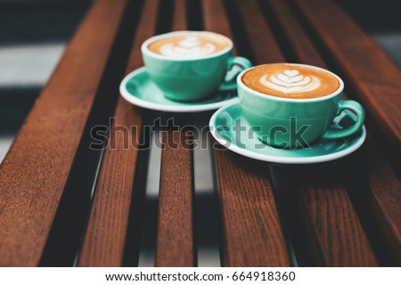 Two cups of cappuccino with latte art on wooden background. Beautiful foam, greenery ceramic cups, stylish toning, place for text. Royalty-Free Stock Photo #664918360
