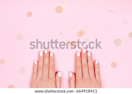 Stylish trendy female pink and blue manicure. Beautiful young woman's hands on pink pastel background with festive multicolored confetti.