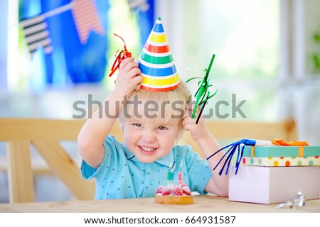 Cute little boy having fun and celebrate birthday party with colorful decoration and cake. Child with sweets, candy, whistle/blower/horn and festive gifts. Preschooler or toddler birthday party.