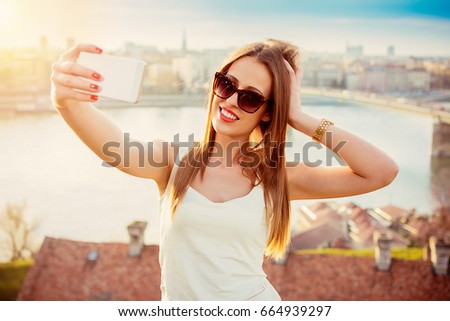 Beautiful happy laughing brunette female taking selfie and enjoying sun with city overview and river Danube in the background