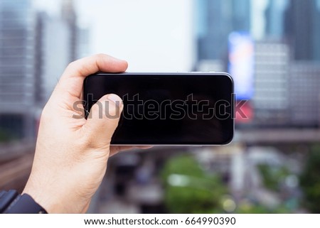 Man uses his Mobile Phone at cityscape background in morning light, close up, capture the moment by a smart phone in my hands. cityscape background. building background. black screen.