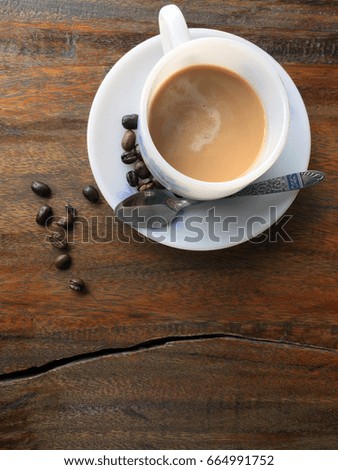 coffee in the white and flower pattern cup with coffee bean on the wooden table. setting of cappuccino in the white cup and a bean like seed of the coffee shrub on the table.